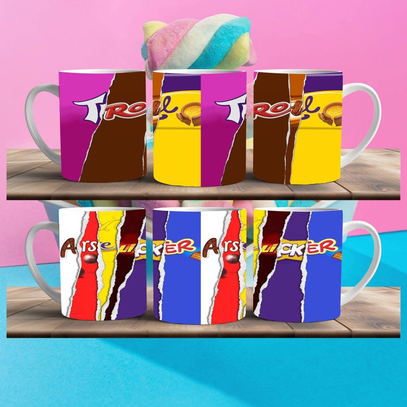 May include: Six white ceramic mugs with different designs. The mugs have a handle on the left side. The designs include a yellow, purple, and brown color scheme with the word "TROLL" and a chocolate bar design. The other mugs have a red, yellow, purple, and blue color scheme with the word "ARSE LICKER" and a chocolate bar design.