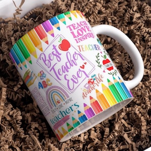 May include: White ceramic mug with a colorful design featuring pencils, rainbows, and the text "Best Teacher Ever". The mug also includes the words "Teach Love Inspire" and "Teacher".