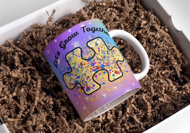 Puede incluir: Una taza de cer&aacute;mica blanca con un fondo degradado morado, azul y amarillo. La taza presenta una gran pieza de rompecabezas amarilla con salpicaduras de pintura de colores y el texto "Let's Grow Together".
