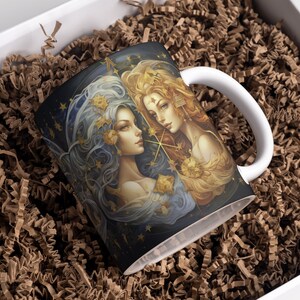 May include: A white ceramic mug with a black and gold design featuring two women with flowing hair and stars. The women are surrounded by a starry night sky.