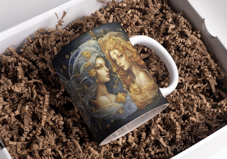 May include: A white ceramic mug with a black and gold design featuring two women with flowing hair and stars. The women are surrounded by a starry night sky.