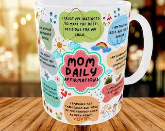 May include: A white ceramic mug featuring colourful, hand-drawn style shapes and text that reads "MOM DAILY AFFIRMATIONS" in the centre, surrounded by various positive statements like "I trust my instincts" and "I am worthy of rest and self-care."
