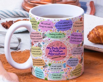 May include: White ceramic mug with a pink, yellow, and blue design featuring positive affirmations. The mug has a large handle and reads "My Daily Dose of Positive Affirmations".