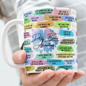 Pode incluir: Caneca de cerâmica branca com um design colorido que apresenta citações inspiradoras e as palavras "Daily Bible Affirmations".