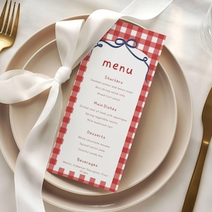 May include: A rectangular menu card with a red and white gingham border and a dark blue bow graphic at the top. The text lists Starters, Main Dishes, Desserts, and Beverages. A white satin ribbon is tied around the menu, which rests on a plate.