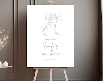 May include: A white bridal shower sign with a gray illustration of two champagne flutes with bubbles. The text on the sign reads "Welcome to Emily's Bridal Shower August 28th, 2024".