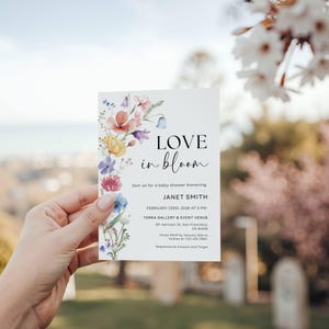 May include: A white baby shower invitation with floral watercolor illustrations in shades of pink, yellow, blue, and purple. The invitation reads "LOVE in bloom" and includes event details.