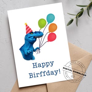 May include: A birthday card featuring a blue dinosaur wearing a party hat and holding colorful balloons. The card reads "Happy Birffday!" in navy blue text. A digital download seal is in the corner.
