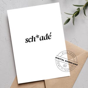 May include: A white card with the word "sch*adé" in black, stylized font. The card is on top of a brown envelope. A circular stamp reads "Digital Download" and "Print It Yourself". Greenery is in the background.