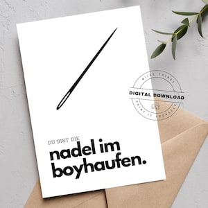 May include: A white card with a black needle illustration and German text that reads "Du bist die Nadel im Boyhaufen." A digital download stamp is in the upper right corner. The card rests on a brown envelope.