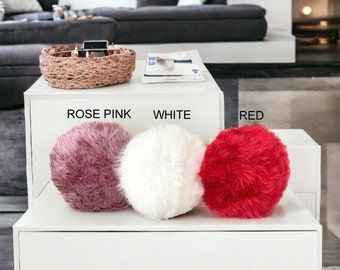 May include: Three fluffy round pillows in rose pink, white, and red colors. The pillows are arranged on a white shelf with the words "ROSE PINK", "WHITE", and "RED" written below each pillow.