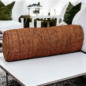 May include: A brown and gold cylindrical pillow with a woven texture. The pillow is resting on a white surface.