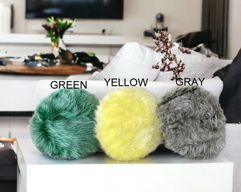 May include: Three round fluffy pillows in green, yellow, and gray colors. The pillows are arranged in a row on a white surface.