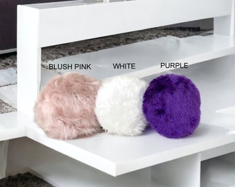 May include: Three round fluffy throw pillows in blush pink, white, and purple. The pillows are sitting on a white shelf with the words "Blush Pink", "White", and "Purple" written below them.