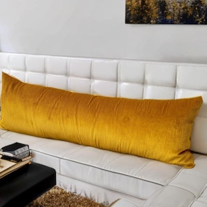 May include: A long, mustard yellow corduroy bolster pillow on a white tufted couch.