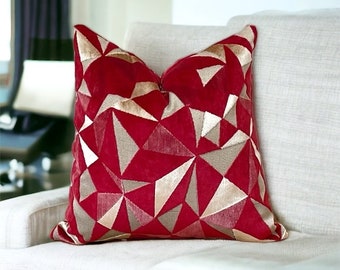 May include: Red velvet cushion with a geometric pattern of gold and pink triangles.