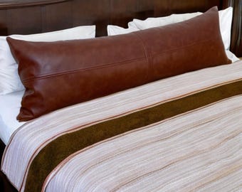 May include: A brown leather body pillow on a white and brown striped bedspread.