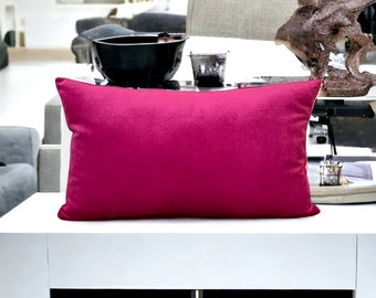 May include: A bright pink rectangular throw pillow on a white coffee table with a black electronic device in the drawer below.