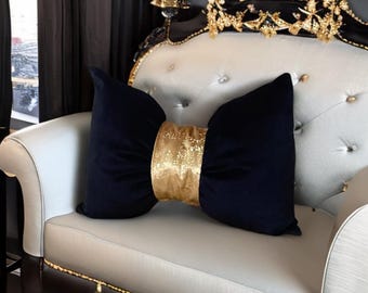 May include: A black velvet pillow with a gold glitter bow. The pillow is sitting on a white couch.