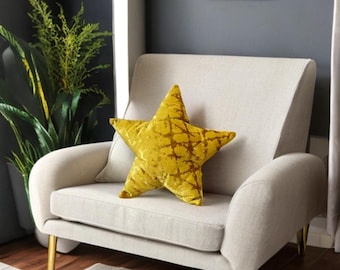 May include: A yellow star-shaped throw pillow with a textured velvet fabric. The pillow is sitting on a light beige armchair with gold legs.