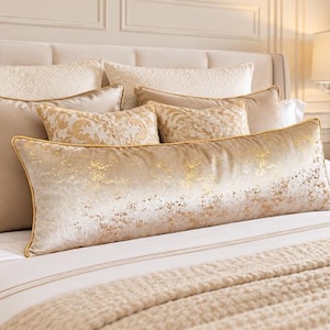 Peut inclure: Un long coussin lombaire rectangulaire en velours couleur champagne avec une texture métallique dorée à l'effet vieilli. Le coussin est bordé d'un passepoil doré sur les bords et est présenté parmi d'autres coussins de lit décoratifs.