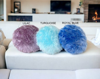 May include: Three round fluffy pillows in lilac, turquoise, and royal blue colors. The pillows are arranged in a row on a white couch.