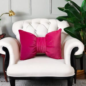 Peut inclure: Un fauteuil blanc avec une garniture noire et un grand coussin en velours rose vif en forme de nœud.