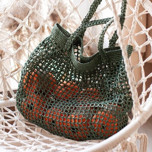 May include: A green crocheted mesh bag with orange fabric inside, sitting in a white macrame hanging chair.