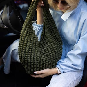 May include: A dark olive green hobo-style bag crafted with a textured, raised bobble stitch pattern. The bag features a single integrated shoulder strap and a slouchy, rounded silhouette, showcasing a dense, uniform knit construction throughout.