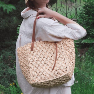 Könnte beinhalten: Eine Frau trägt einen Strohhut und ein weißes Hemd und hält eine gehäkelte Tragetasche mit braunen Lederriemen. Die Tasche hat einen gewellten Rand und ein gewebtes Muster.