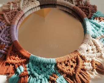 Peut inclure: Un miroir rond avec un cadre en macramé dans des tons de brun, beige, blanc, turquoise et violet. Le cadre est orné d'une frange sur tout le pourtour.