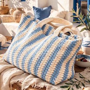 May include: A blue and cream striped tote bag with woven handles rests on a wooden table. The bag is the focal point of a scene set outdoors, with a view of the sea and a white building with blue painted details. The bag is made of a woven material.