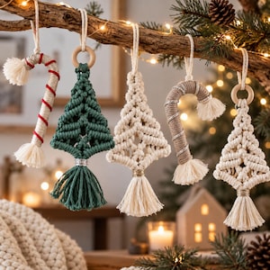 May include: Five macrame ornaments hanging from a branch. Two are candy canes, one wrapped in red and white cord, the other in tan and silver. Three are triangular trees, one dark green and two off-white, each featuring a wooden ring and tassel.
