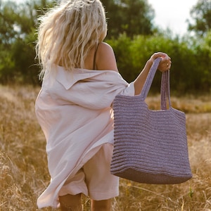 Può includere: Una borsa tote rettangolare color lavanda con una superficie intrecciata testurizzata e due spallacci abbinati. La borsa presenta un motivo strutturato a coste orizzontali su tutto il corpo, offrendo un aspetto coerente e uniforme.