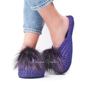 May include: Purple crochet slippers with large, fluffy, dark purple fur accents. The slippers are a solid, deep purple color and have a woven texture. The text "I Love Create" is visible on the slippers.