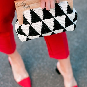 Op de afbeelding: Een clutch met een zwart-wit geometrisch patroon en een houten handvat. De tekst "I Love Create" staat op het houten handvat. De persoon draagt een rode broek en rode pumps met spitse neus.