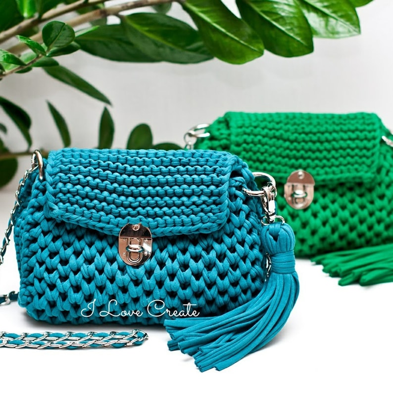 Puede incluir: Dos bolsos de mano de crochet con correas de cadena plateadas y borlas. El bolso de mano de la izquierda es azul turquesa y el bolso de mano de la derecha es verde. Ambos bolsos de mano tienen un cierre plateado.