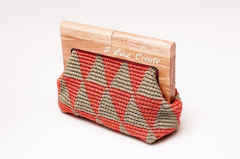 Op de afbeelding: Handgemaakte clutch met een houten frame. De macram&eacute; tas heeft een geometrisch patroon in koraal en beige. Het houten frame is gegraveerd met de woorden "I Love Create".