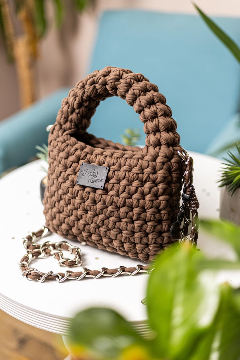 Op de afbeelding: Een bruine gehaakte handtas met een kettingband en een klein leren label met de tekst "I Love Knit"