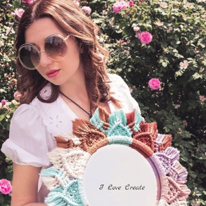 May include: A woman with brown hair and round sunglasses holds a macrame wall hanging with a white circle in the center. The wall hanging has a variety of colors including brown, white, blue, and purple. The text "I Love Create" is written on the white circle.