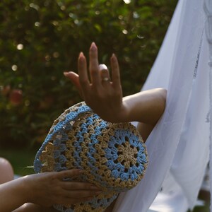 May include: A woman wearing a blue and brown crocheted sun hat while relaxing in a hammock.
