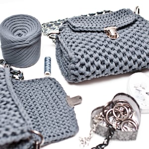 Puede incluir: Dos bolsos de mano de crochet grises con un cierre de plata y una correa de cadena. Tambi&eacute;n se muestra una bola de hilo gris y una bobina de hilo.