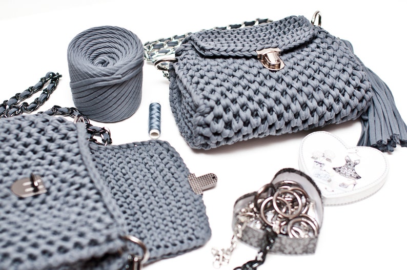 Puede incluir: Dos bolsos de mano de crochet grises con un cierre de plata y una correa de cadena. Tambi&eacute;n se muestra una bola de hilo gris y una bobina de hilo.