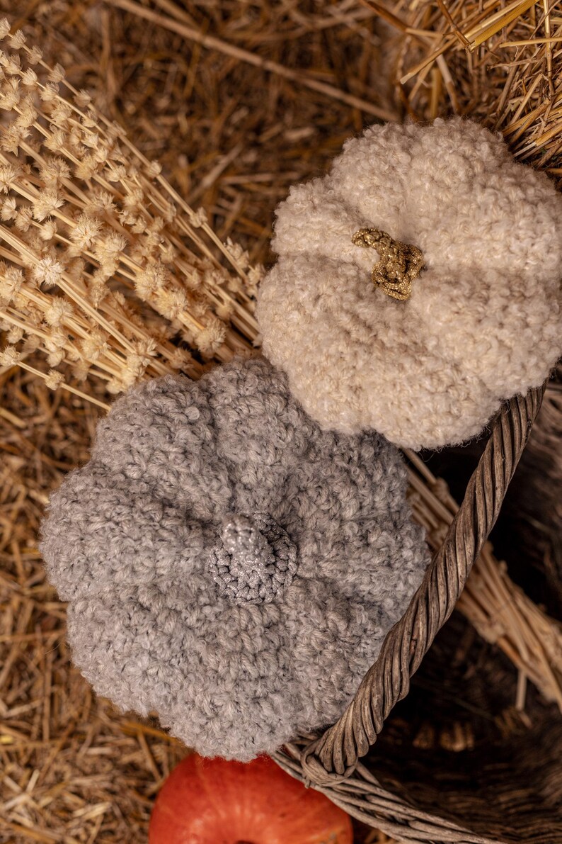 May include: Two gray and white crocheted pumpkin-shaped hats in a wicker basket with dried flowers.
