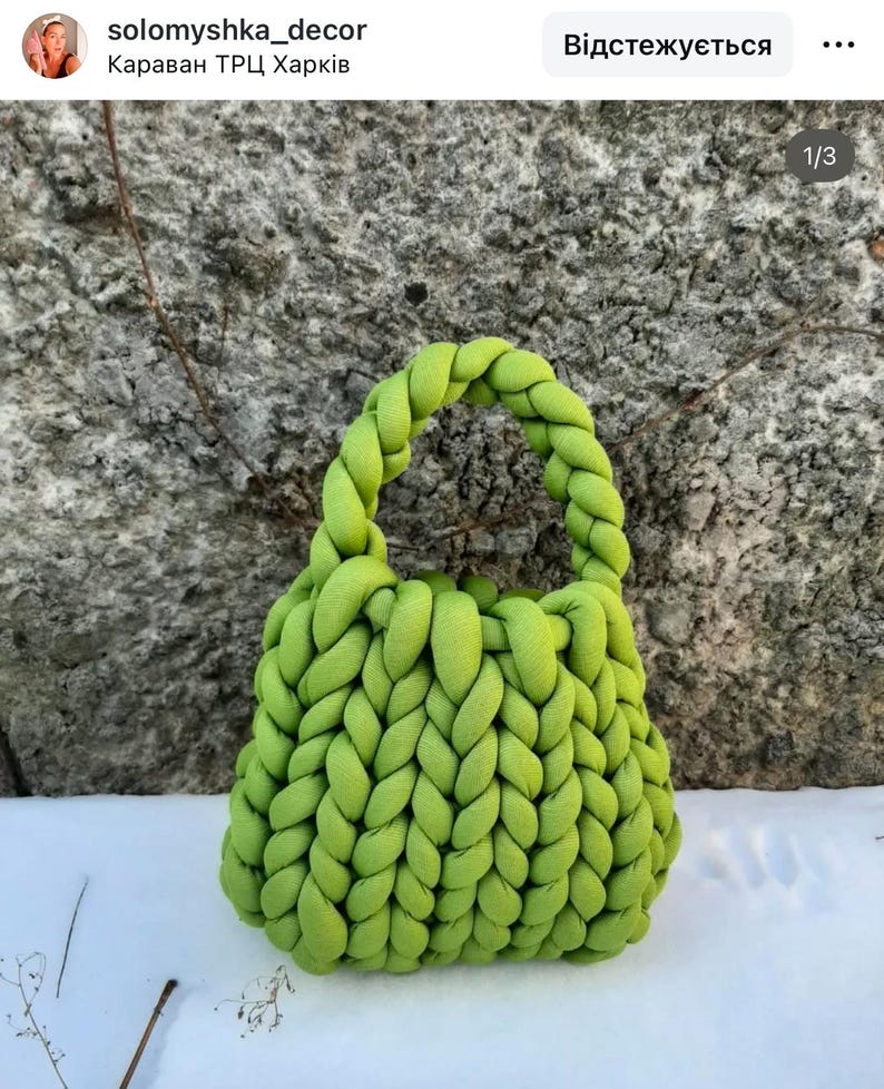 Puede incluir: Una bolsa de mano de punto de color verde brillante con un asa trenzada. La bolsa est&aacute; hecha de hilo grueso y tiene una textura gruesa.