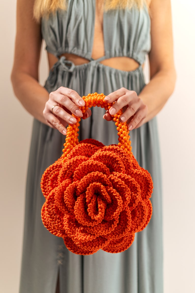 May include: A large orange crocheted flower-shaped handbag with a bright orange beaded handle.