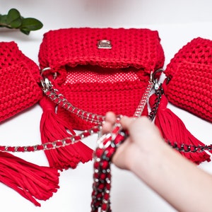 Puede incluir: Tres bolsos de mano de crochet rojo con cadenas plateadas y borlas. Los bolsos est&aacute;n dispuestos en fila con el bolso del medio abierto.