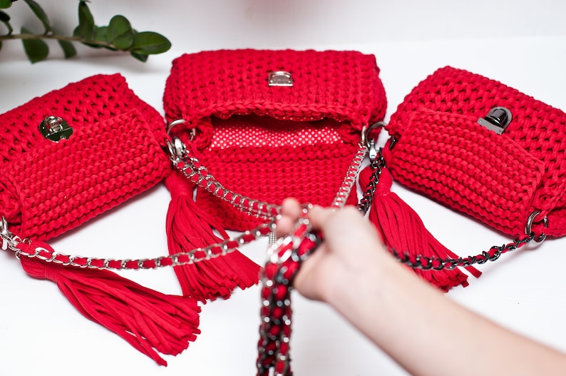 Puede incluir: Tres bolsos de mano de crochet rojo con cadenas plateadas y borlas. Los bolsos est&aacute;n dispuestos en fila con el bolso del medio abierto.