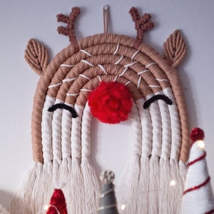 May include: A brown and white yarn reindeer rainbow wall hanging with a red pom-pom nose. The rainbow is made of yarn and has a fringe at the bottom.