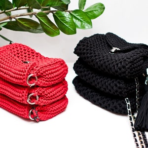Puede incluir: Dos bolsos de crochet, uno rojo y otro negro, con correas de cadena y borlas. Los bolsos est&aacute;n apilados uno encima del otro.